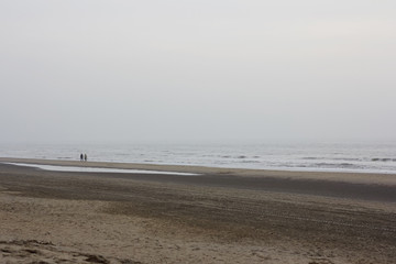 Silhouettes of two people walking along the cold winter shore of the north sea at sunset