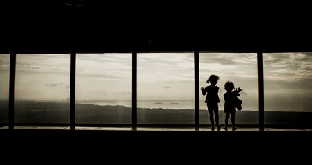 Fototapeta premium Two young girls looking out the high skyscraper window, panoramic view over the cityscape.