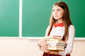 beautiful young school girl in school uniform standing with books in her hands