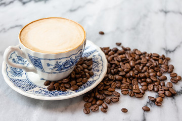 Coffee milk in a cup with coffee bean, rose patterned ceramic cup, on marble table in the morning light.