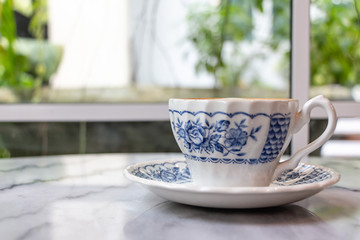 Coffee milk in a cup, rose patterned ceramic cup, on marble table in the morning light.