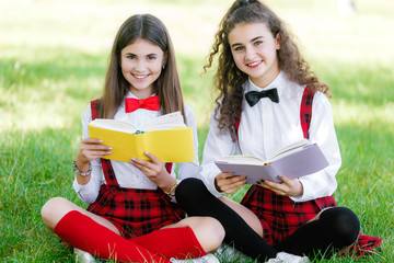 Fototapeta premium two funny schoolgirls sit on the grass and read books. Girls, girlfriends, sisters are taught lessons in nature