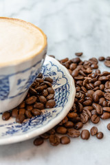 Coffee milk in a cup with coffee bean, rose patterned ceramic cup, on marble table in the morning light.