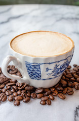 Coffee milk in a cup with coffee bean, rose patterned ceramic cup, on marble table in the morning light.