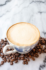 Coffee milk in a cup with coffee bean, rose patterned ceramic cup, on marble table in the morning light.