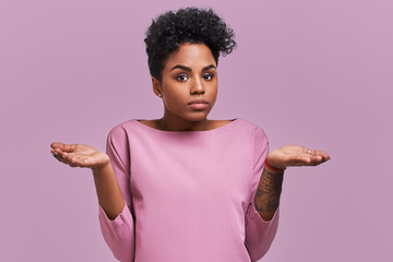 Uncertain African American female with dark skin, shruggs shoulders and asks something, has...