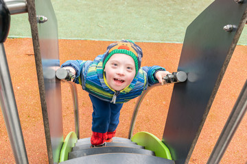 Defect,childcare,medicine and people concept- young boy with a down syndrome who is playing in a playground.