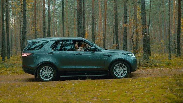 TRACKING Caucasian couple with a pet dog driving on a forest road in a modern SUV. 4K UHD