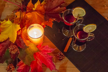 Autumn relaxation concept. Two glasses of mulled wine and a burning candle surrounded by maple leaves on a wooden table..