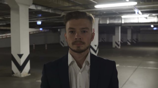 Businessman in black corporate suit walking down dark empty dangerous parking lot and thinking about Something Sad or concentrated on his current work projects. Seems He is very busy and need some rel