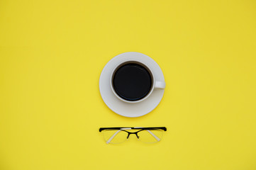coffee Cup and glasses on yellow background with copy space top veiw