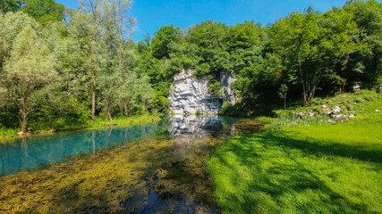 Obraz premium Krupa Spring (Izvir Krupa) in Bela Krajina, southern Slovenia, is a big karst spring below rock wall. It is protected as natural heritage and special habitat of water spices.