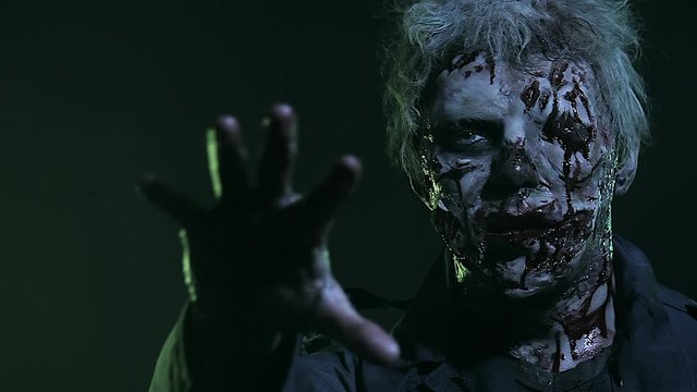 Horror zombie. Halloween party. Close-up portrait of a horrible scary zombie man in smoke.