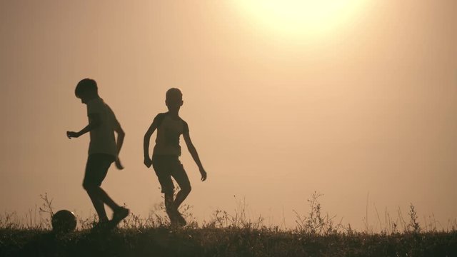 Two boys playing soccer at sunset. Silhouette of children playing with a ball at sunset. The concept of a happy family