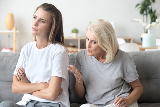 Controlling elderly mother scolding adult daughter having serious conversation with her, stubborn young woman sit back to mom, not listening to strict aged parent lecturing her or giving advice