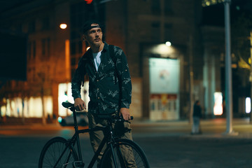 Fototapeta premium Cyclists standing on the road aside his classic bike while watching night city