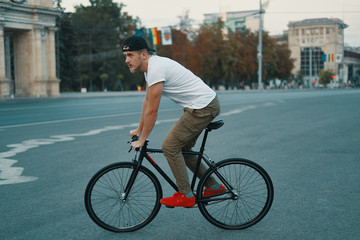 Fototapeta premium Young modern man cycling on a classic bike on the city road