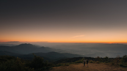 Two Young man standing on top of cliff in summer mountains at sunset and enjoying view of nature with twlight.