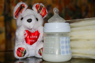 baby bottle with fresh expresed milk, frozen breastmilk in storage bags and soft toy mouse