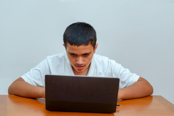 Teenager with laptop sitting at table and studying at home. Fashion portrait of teen black hair handsome boy in office. Young businessman using a laptop.