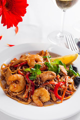 Rice noodles with shrimps in sauce on a white plate, close up