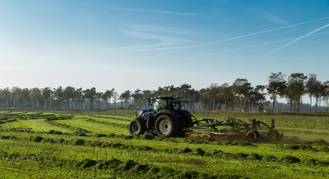 Een boer is met zijn trekker het gemaaide gras aan schudden