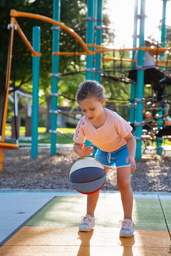 A girl playing with a basketball at a park. 