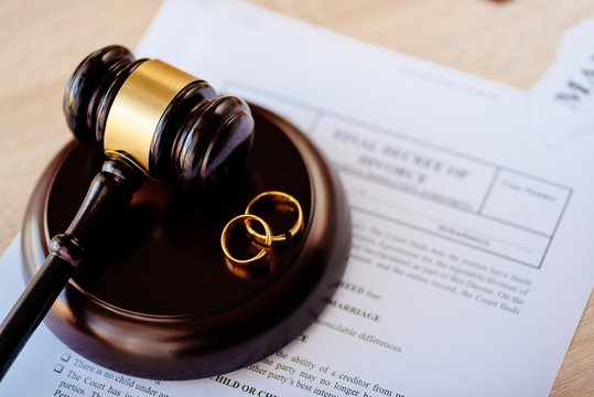 Divorce decree in and two broken wedding rings on judge gavel.