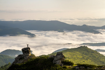 Small silhouette of tourist with raised arms on rocky formation on mountain valley filled with...
