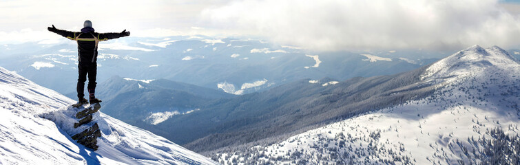 Silhouette of alone tourist standing on snowy mountain top in winner pose with raised hands...