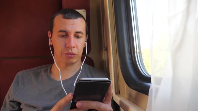 man listening to the music on the train rail car coupe compartment travel. slow motion video. man with a smartphone at the window of a lifestyle train in a car travel internet social media web. man