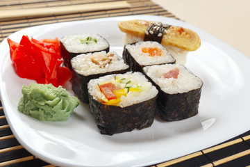 Sushi and rolls with ginger and wasabi on a black bamboo mat close up.