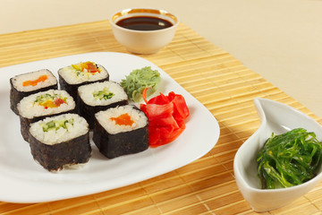 Assorted sushi, hiyashi wakame salad and soy sauce on a bamboo mat close up.