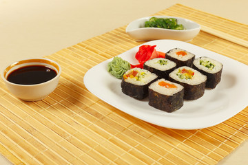 Sushi set, hiyashi wakame salad, soy sauce with ginger and wasabi on a bamboo mat close up.