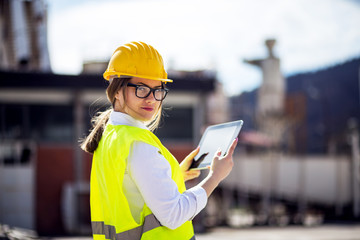 Female architect wearing reflective vest and hardhat using tablet