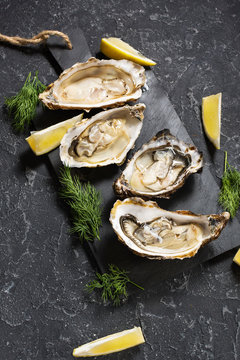 Opened Oysters with lemon on dark stone background