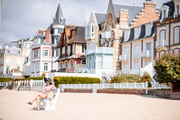 Woman sitting on the bench enjoying beautiful view on the beach in Trouville city, famous french resort in Normandy - obrazy, fototapety, plakaty