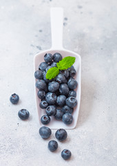 Fresh organic raw blueberries in white scoop spoon with leaf on stone kitchen table background
