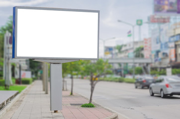 Fototapeta premium duży pusty billboard biały ekran LED poziomy wybitny w mieście po stronie ścieżki ruch drogowy do wyświetlania szablonu tekstu reklamy promocja nowej marki na zewnątrz z zielonym drzewem.