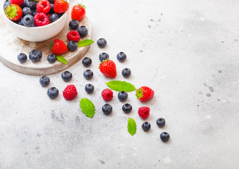 Fresh raw organic berries isolated in white ceramic bowl plate on round wooden board. Top view. Strawberry, Raspberry, Blueberry and Mint leaf