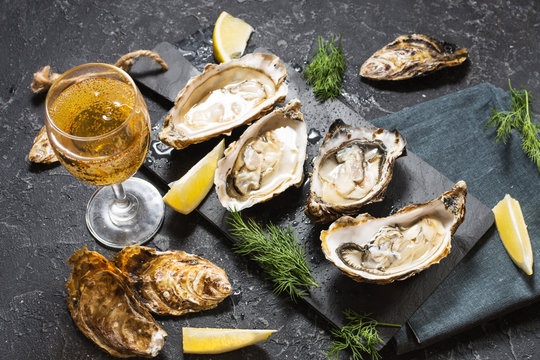Opened Oysters and glass of white wine on dark texture background