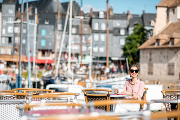 Young woman enjoying coffee sitting at the cafe outdoors near the harbour in Honfleur old town, France