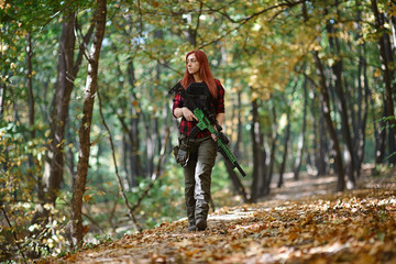 Cute girl with red hair and rifle in her hands on the background of trees