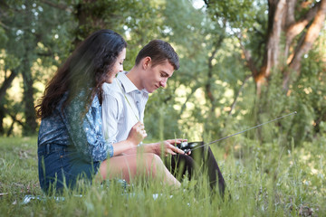 young couple sitting on the grass in the forest and looking on sunset, listen to radio, summer nature, bright sunlight, shadows and green leaves, romantic feelings