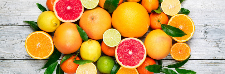 Fresh citrus fruits background. Orange, grapefruit, lemon, lime, tangerine. Mix citrus fruits with leaves. Long web format