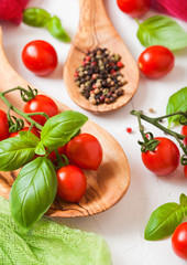Organic Cherry Sugardrop Tomatoes on the Vine with basil in oilve wood plate and spoon with pepper on white kitchen background.