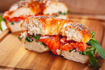 Bagel with cream cheese, smoked salmon and arugula salad cut in half on wooden board. Close up