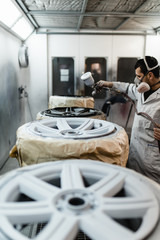 Man with protective clothes and mask painting car parts using spray compressor. Selective focus.