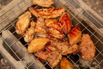 Spicy chicken wings and legs grilling with hot flames.