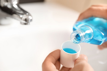 Man pouring mouthwash from bottle into cap in bathroom, closeup. Teeth care - obrazy, fototapety, plakaty